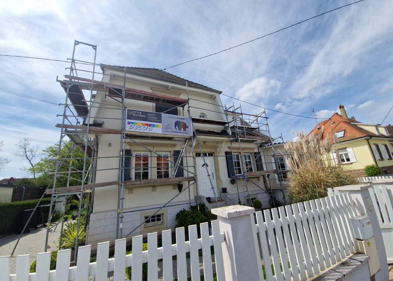 Avant - Facade grande maison Maison en rénovation avec échafaudages et pelouse verte devant, ciel bleu.
