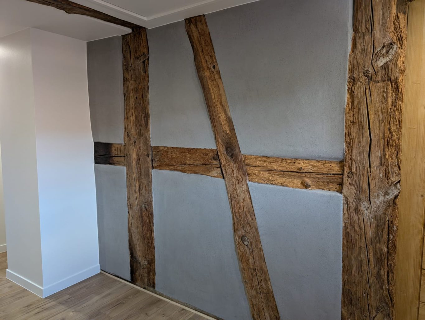 Après - Mur colombage Mur intérieur avec poutres en bois apparent et surface grise.