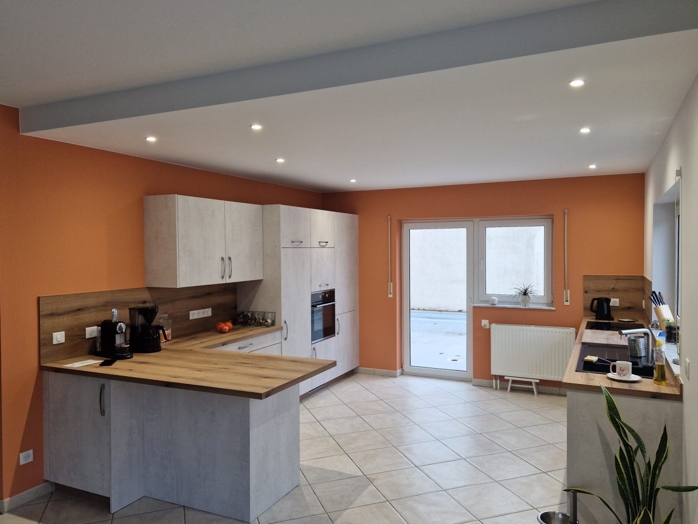 Après - Cuisine Cuisine moderne avec murs orange, comptoir en bois et sol carrelé. Fenêtre à gauche.