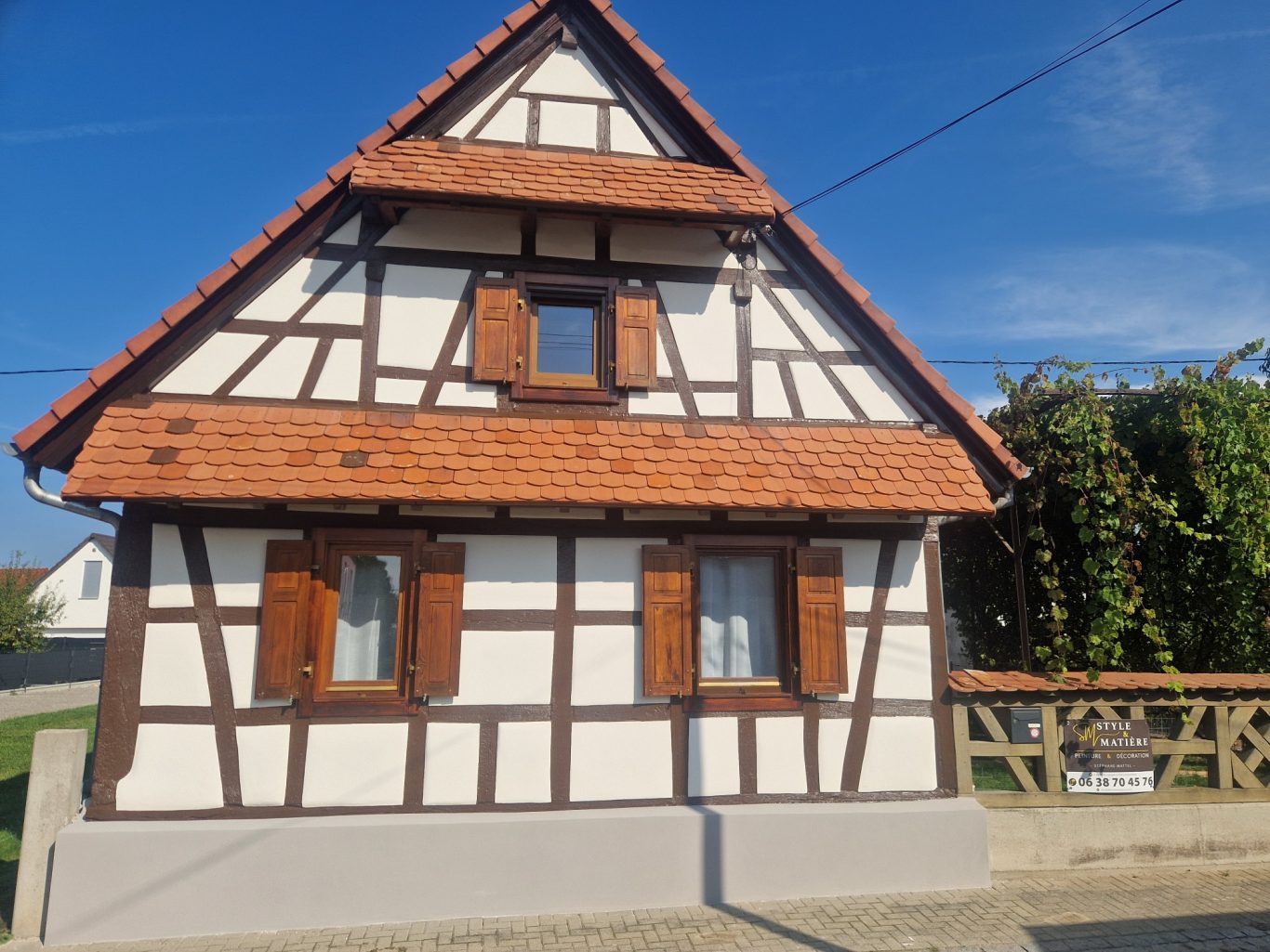 Après - Facade colombage Maison à colombages avec fenêtres à volets en bois, sous un ciel bleu.